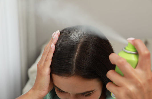 woman spraying dry shampoo on her brown hair roots