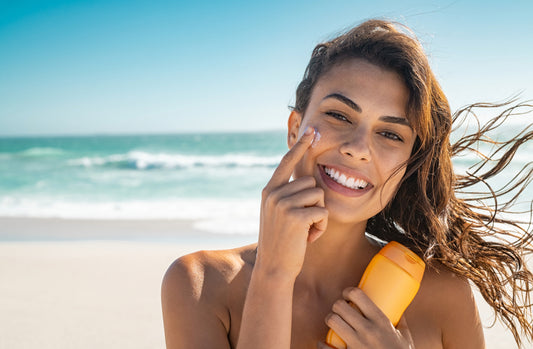 smiling woman holding a sunscreen bottle putting sunscreen on her face